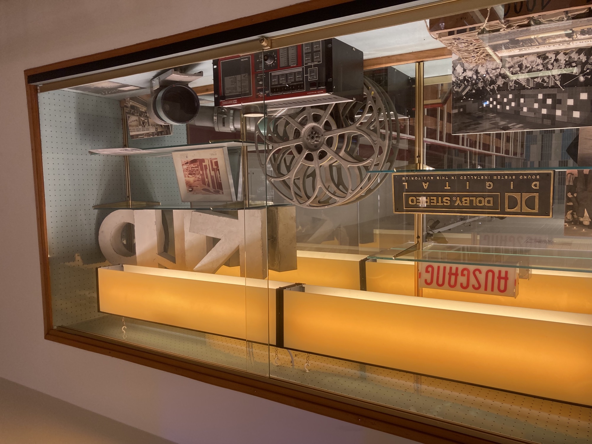 Glasvitrine mit Relikten aus der Vergangenheit des Kinos, zB ein altes „Ausgang“-Schild, eine Filmspule und ein Dolby-Stereo-Digital-Schild