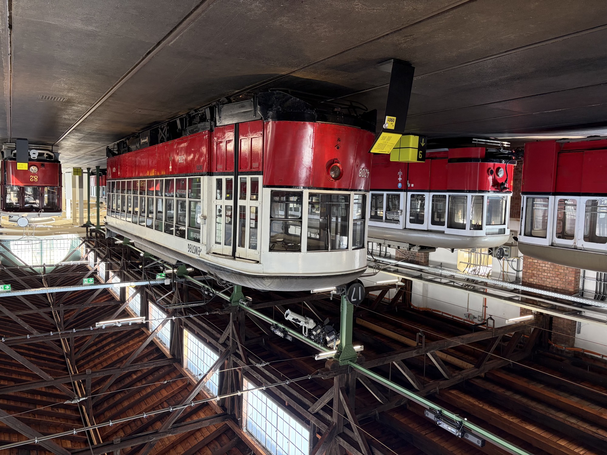 im Zentrum des Bildes eine Strassenbahn im klassischen Wiener Farbschema, unten rot, oben weiß gestrichen, die Straßenbahn trägt die Nummer 17, davor steht ein gelbes Infoschild, das Gebäude ist am Boden von Schienen durchzogen, das Dach besteht aus dunklen Holzbalken, der Raum wird durch große Fenster im Dach von oben beleuchtet