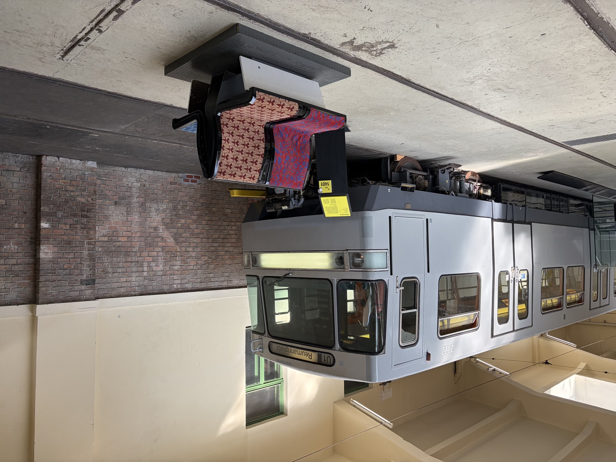 silbergrauer U-Bahn-Wagen mit dem Zielschild U1 Reumannplatz, davor eine Sitzbank mit verschiedenfarbigen Mustern